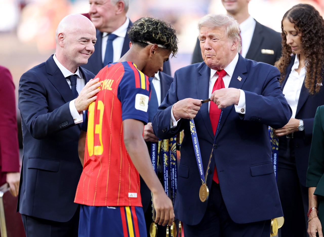 Donald Trump placing a gold FIFA World Cup 2026 medal over a Spain player wearing number 13, with Gianni Infantino smiling beside them.