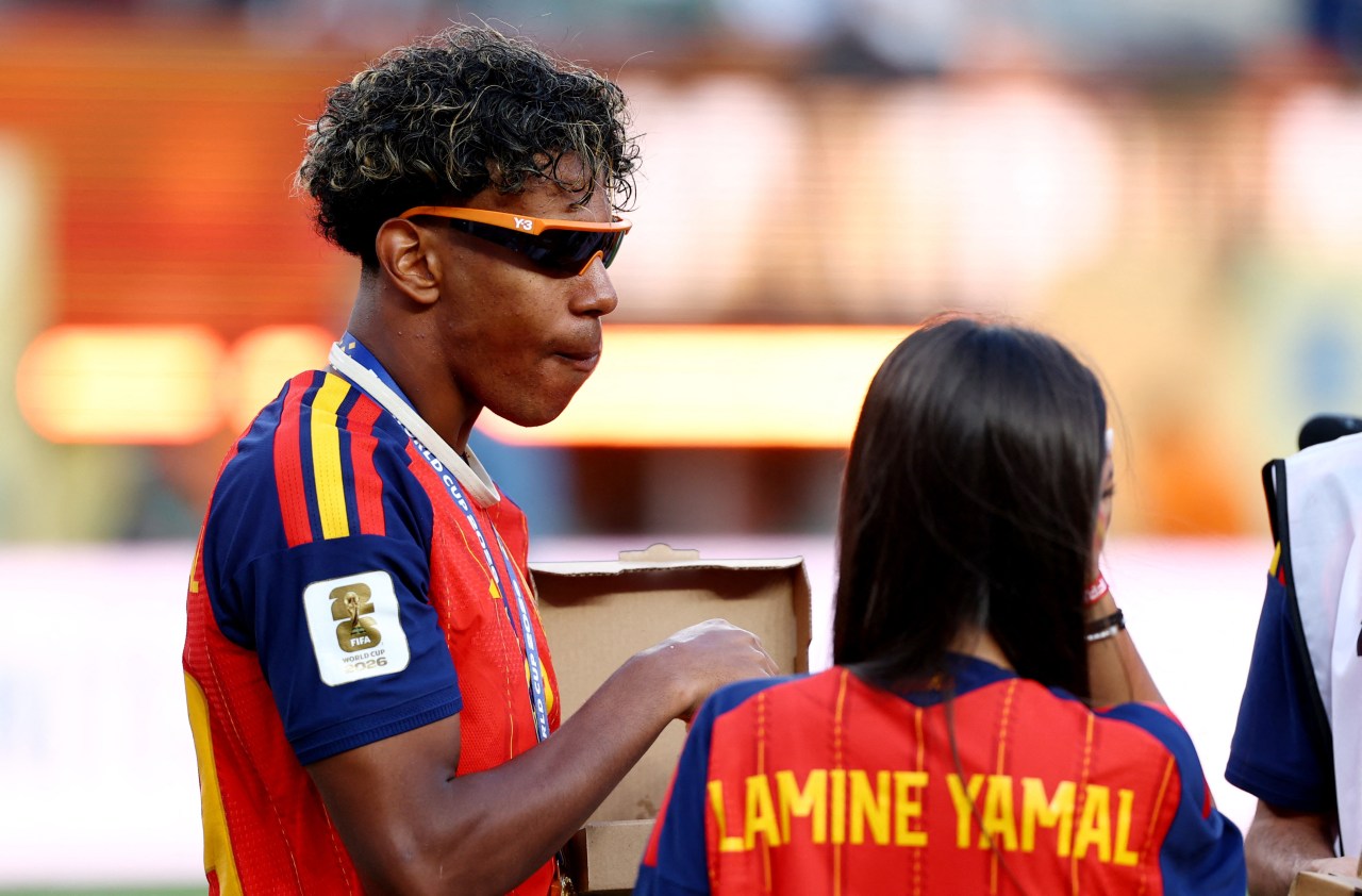 Lamine Yamal in Spain kit and orange sunglasses with a World Cup medal, standing next to a person wearing a jersey printed with his name.