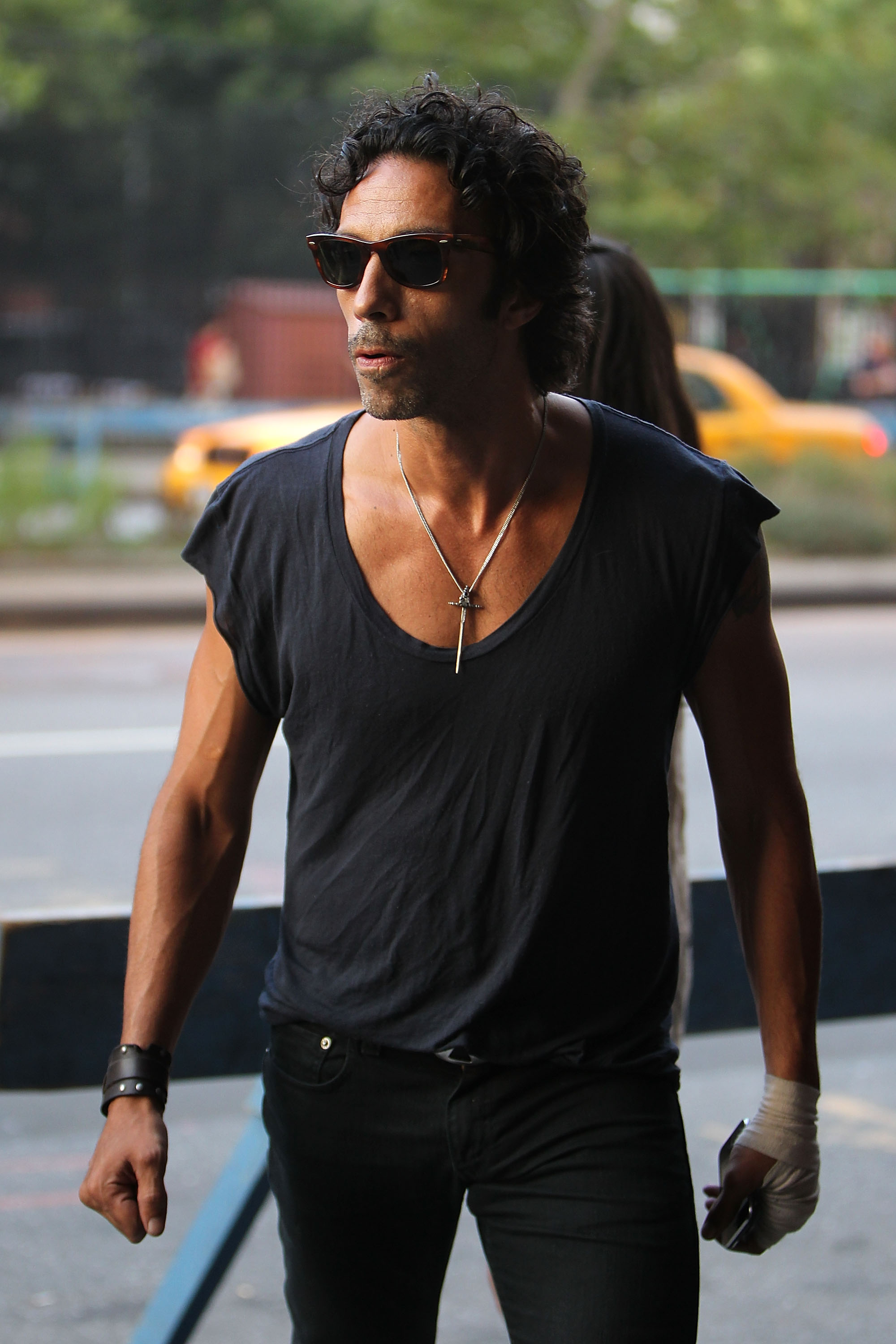 Carlos Leon wearing a black scoop-neck T-shirt and sunglasses walking on a New York City street.