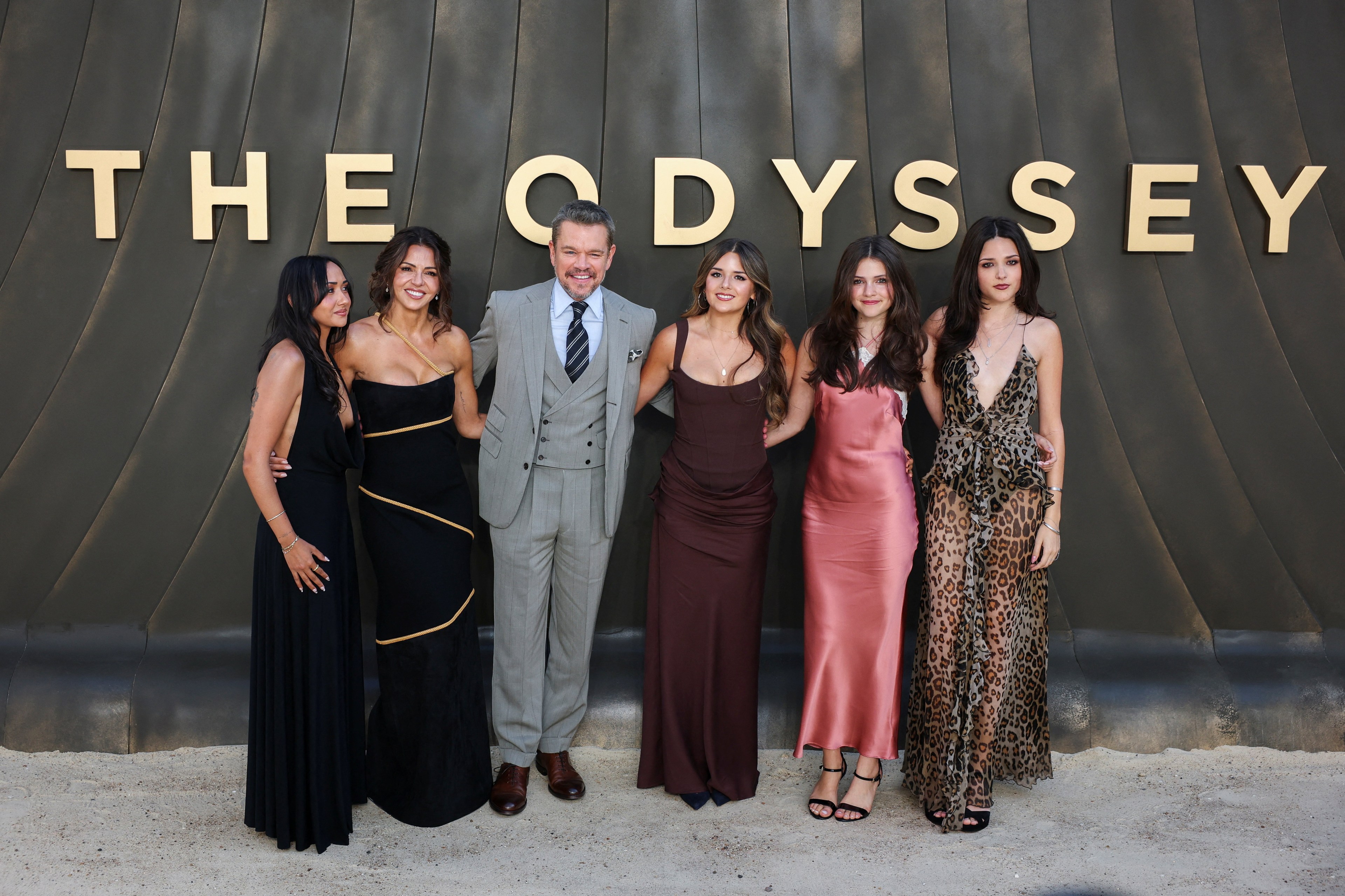 Matt Damon poses with his wife Luciana and their four daughters in front of a large gold 'The Odyssey' sign at a London premiere.