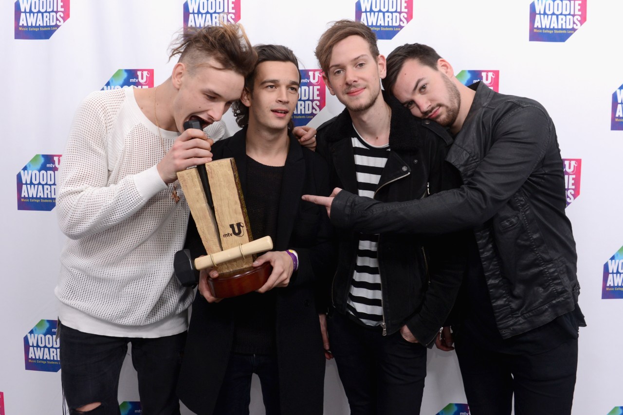 Four young men pose with a wooden Woodie Award trophy in front of an mtvU Woodie Awards step-and-repeat backdrop.