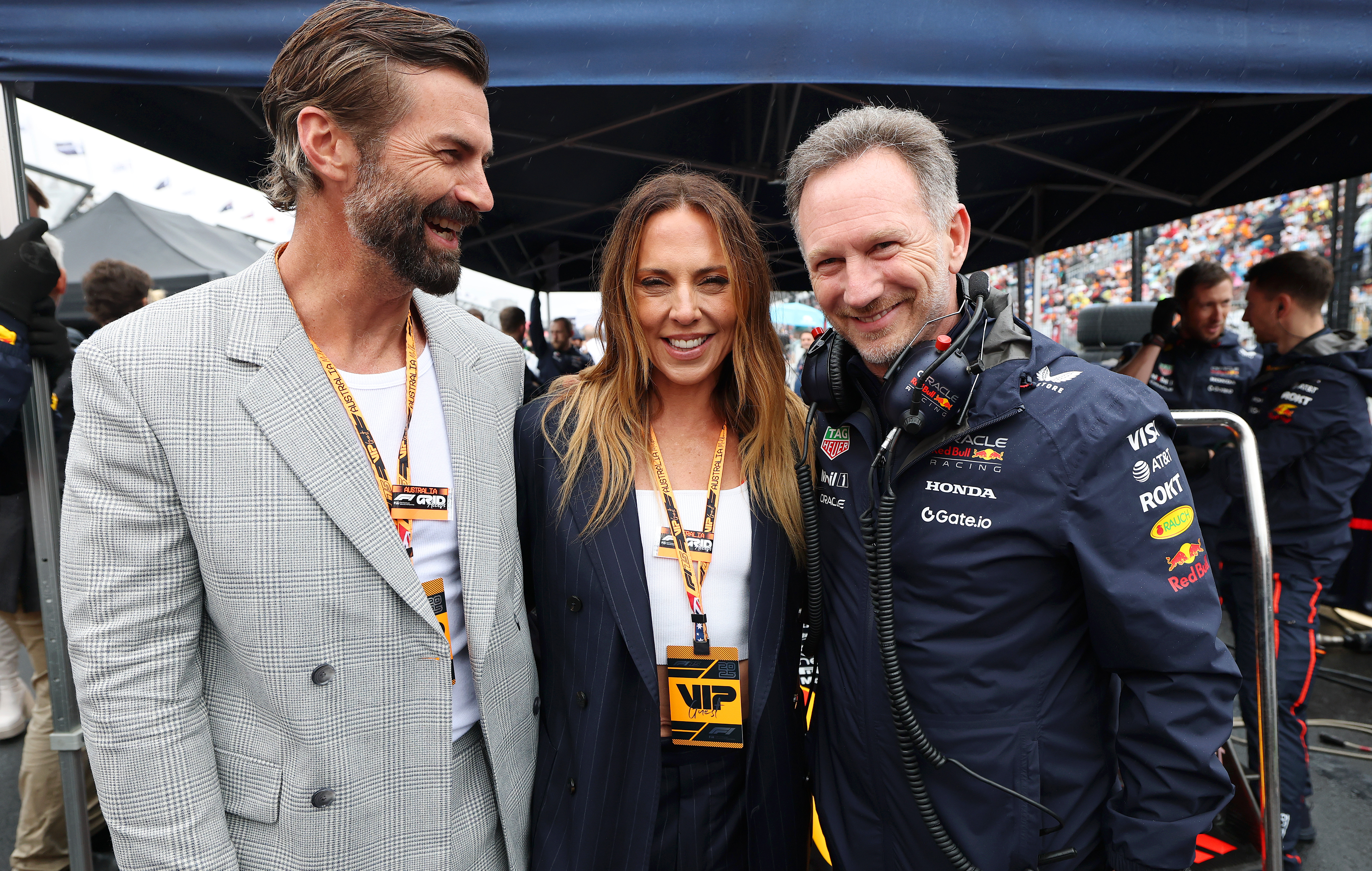 Mel C and Chris Dingwall smile with Christian Horner, wearing a Red Bull Racing jacket, on the F1 grid in Melbourne.