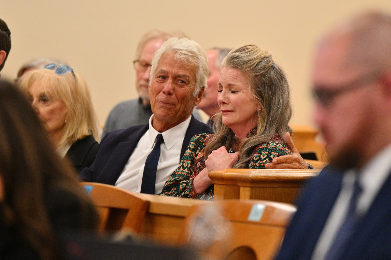 A man and woman seated in a courtroom both appear tearful, with the woman clasping her hands to her chest and closing her eyes.