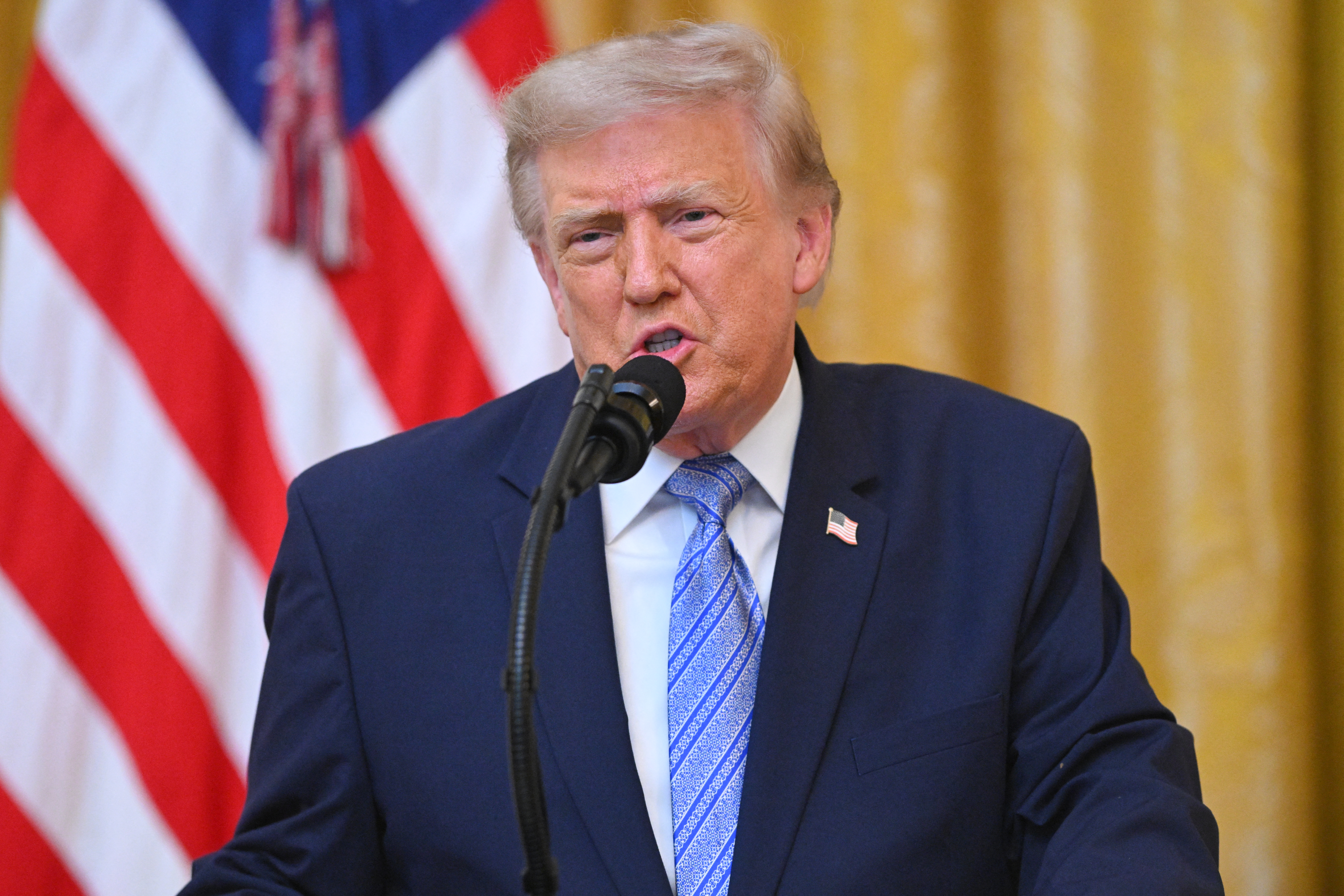Donald Trump speaking at a podium in the East Room of the White House