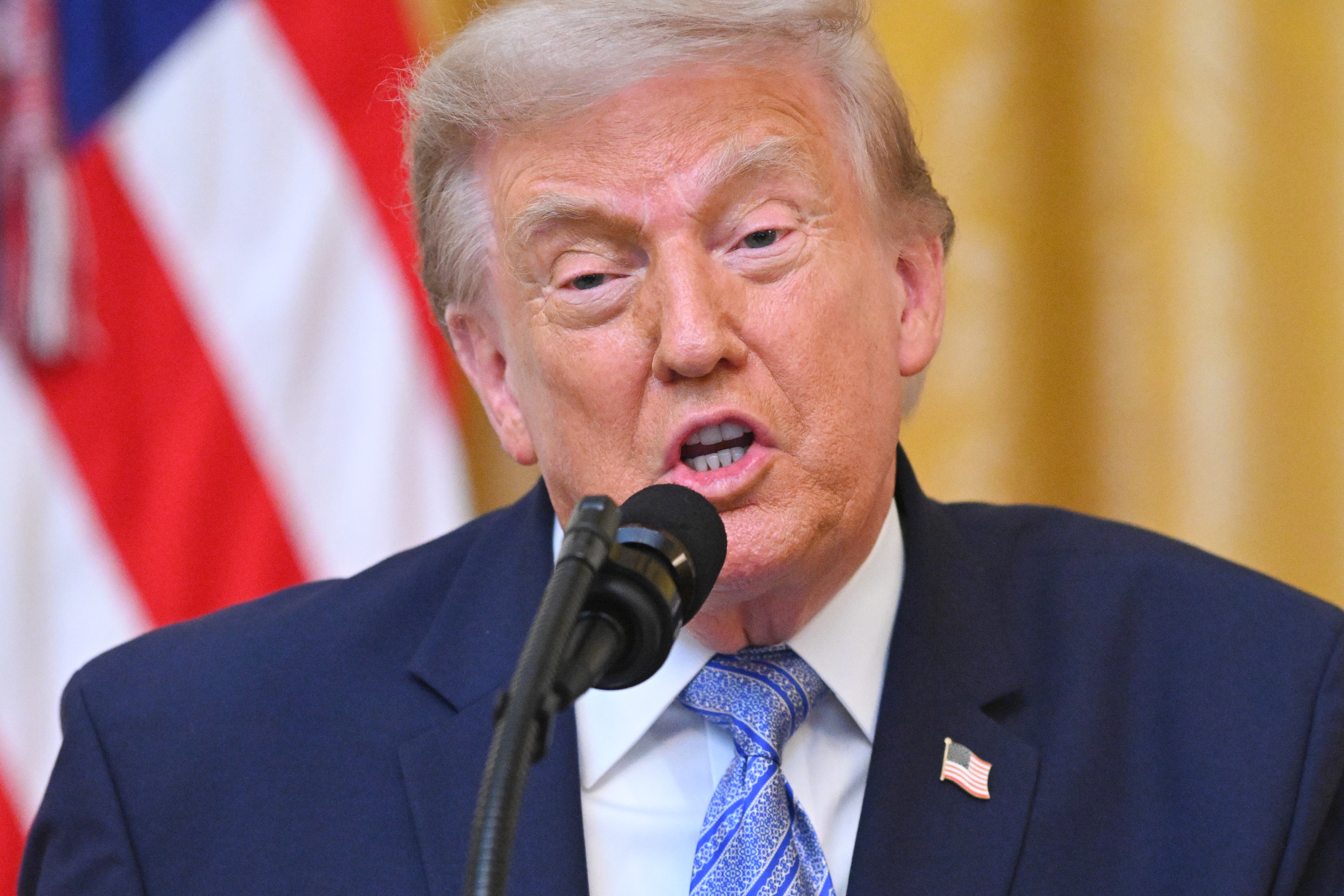 President Donald Trump speaking at a podium in the East Room of the White House