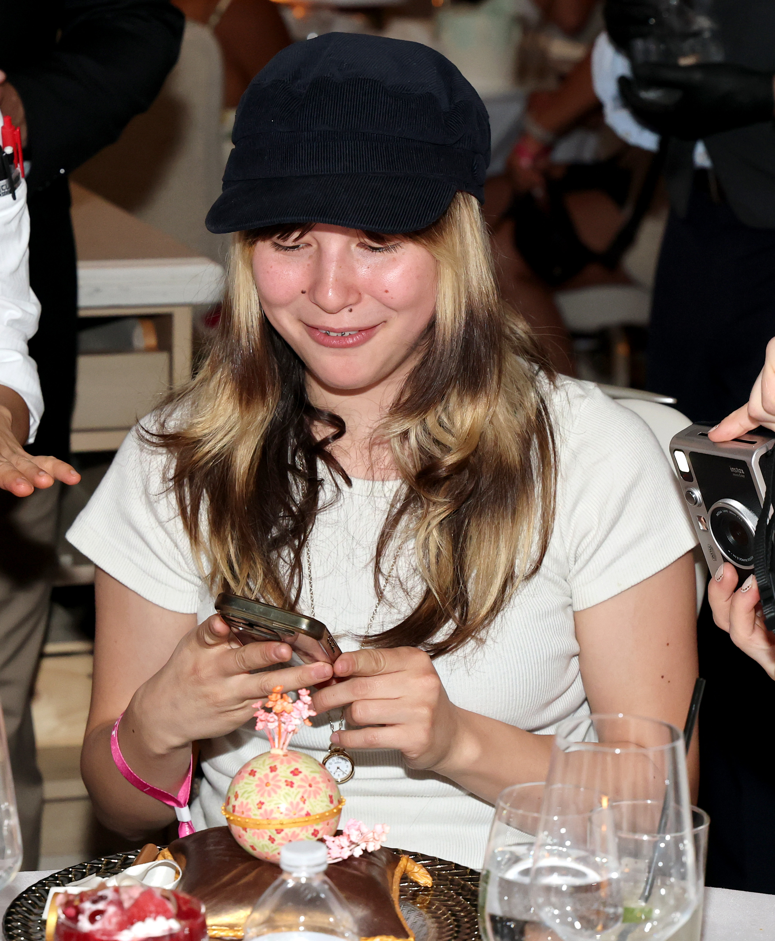 Alysa Liu smiling and reacting to a chocolate sculpture at a VIP dinner, with Amber Glenn photographing the moment beside her