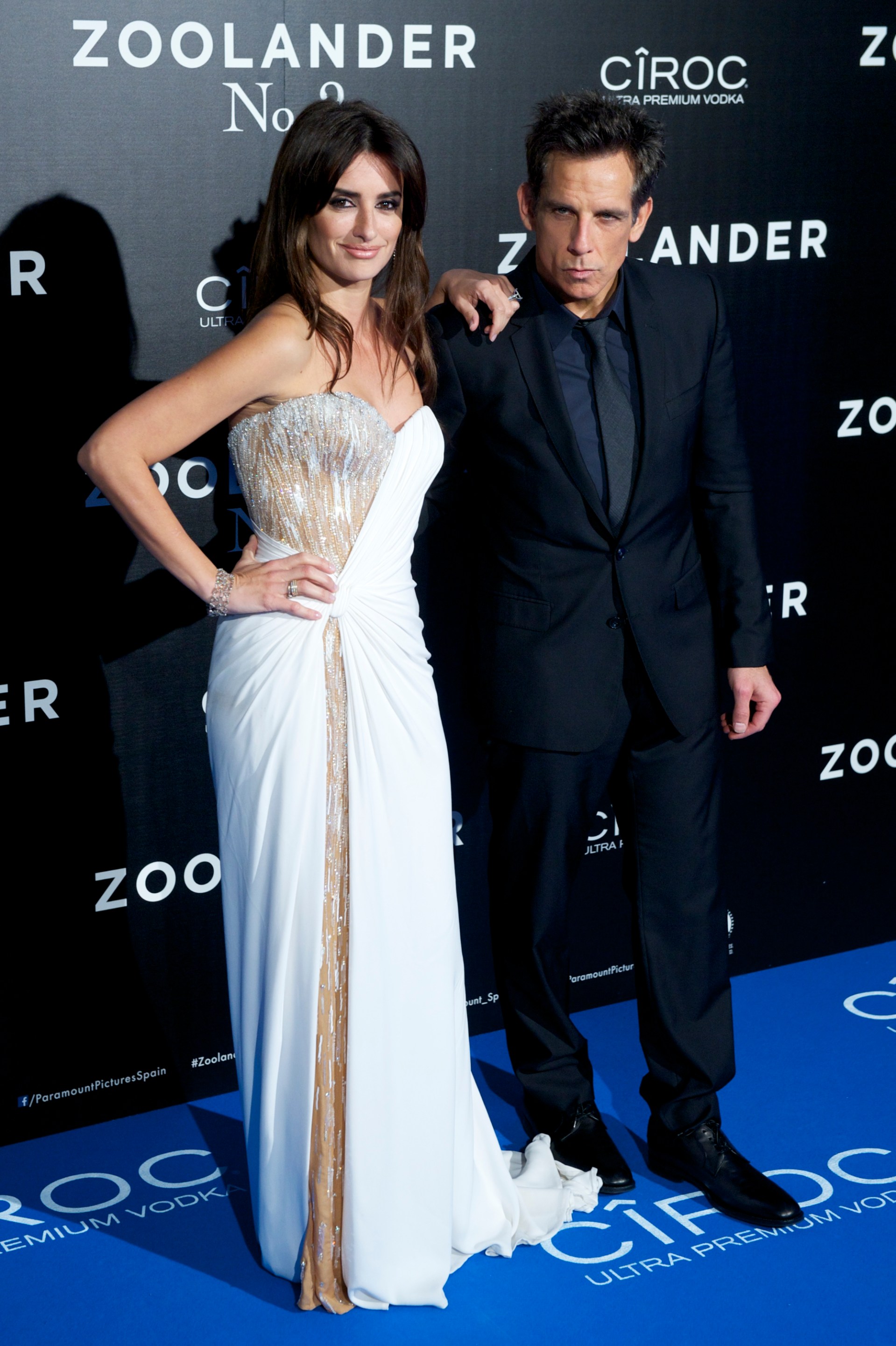Penelope Cruz in a white strapless gown and Ben Stiller in a black suit pose together in front of a Zoolander No. 2 step-and-repeat backdrop.