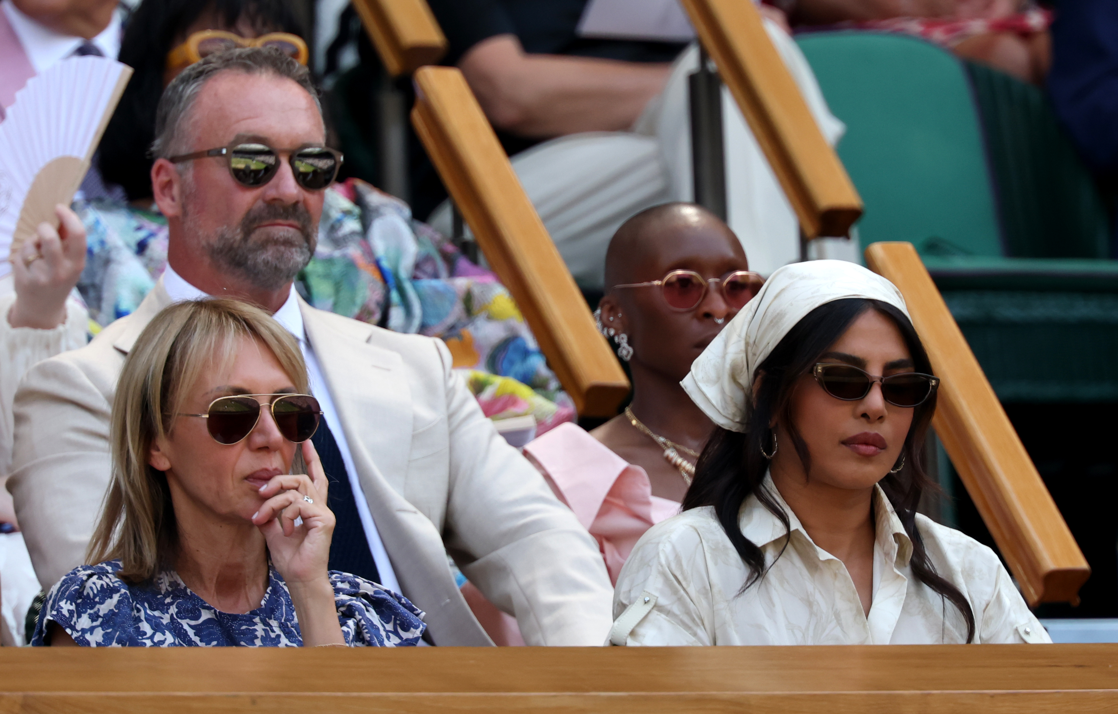 Sahar Hashemi and Priyanka Chopra Jonas seated in the Wimbledon Royal Box, surrounded by other spectators wearing sunglasses on a sunny day.