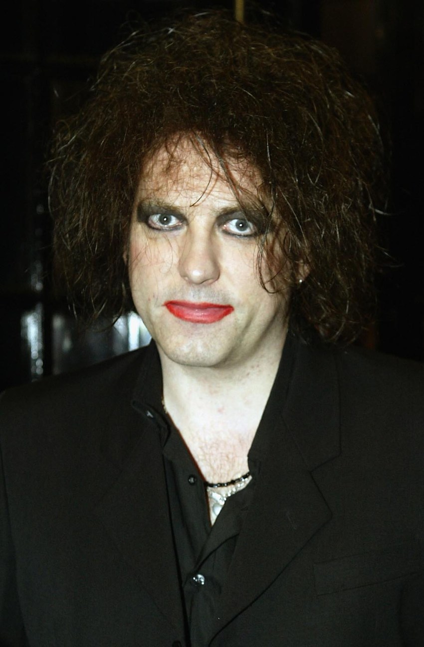 Robert Smith with teased dark hair, heavy eye makeup, and red lipstick, wearing a black blazer at the Q Awards 2003 in London.