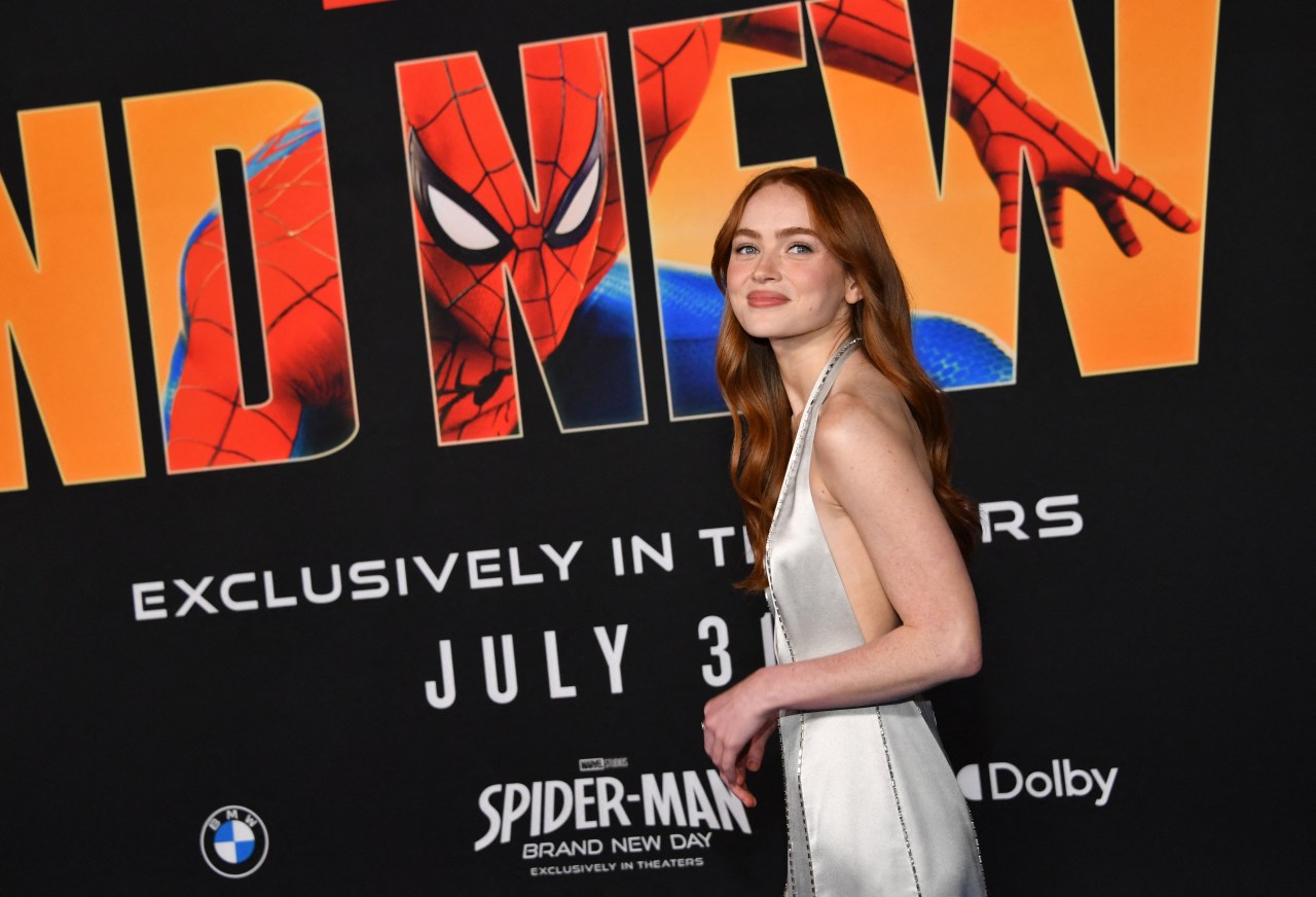 Sadie Sink in a silver satin gown posing in front of a Spider-Man: Brand New Day premiere backdrop at the Dolby Theatre.