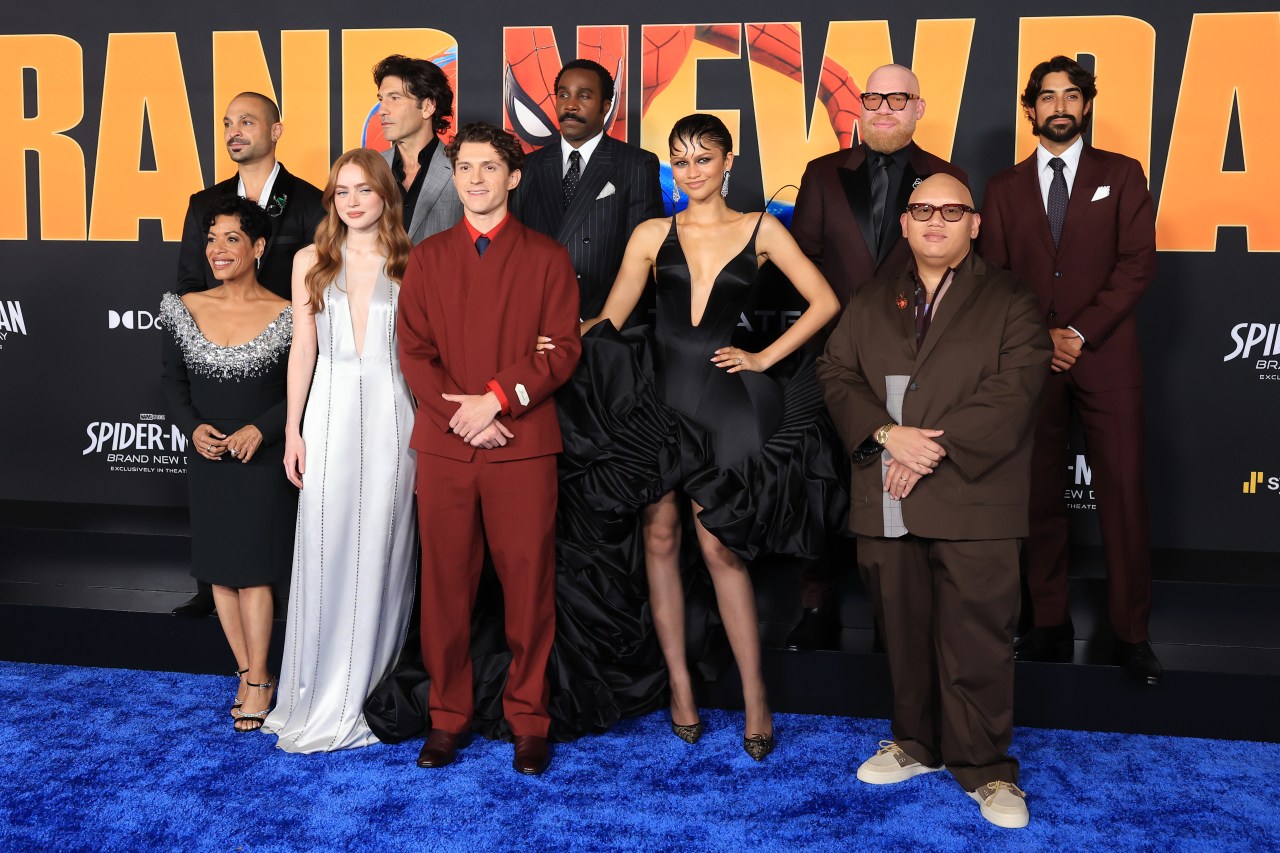 Large group of actors and filmmakers in formal attire pose together on a blue carpet in front of a Spider-Man: Brand New Day premiere backdrop.
