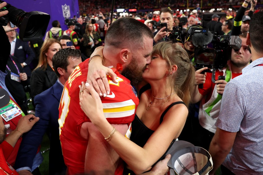 Travis Kelce in a red Kansas City Chiefs jersey kisses Taylor Swift on the crowded field after Super Bowl LVIII at Allegiant Stadium.