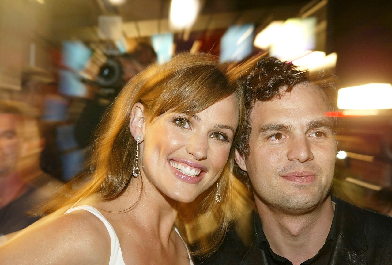 A smiling woman and a man with curly hair posing closely together at a film premiere.