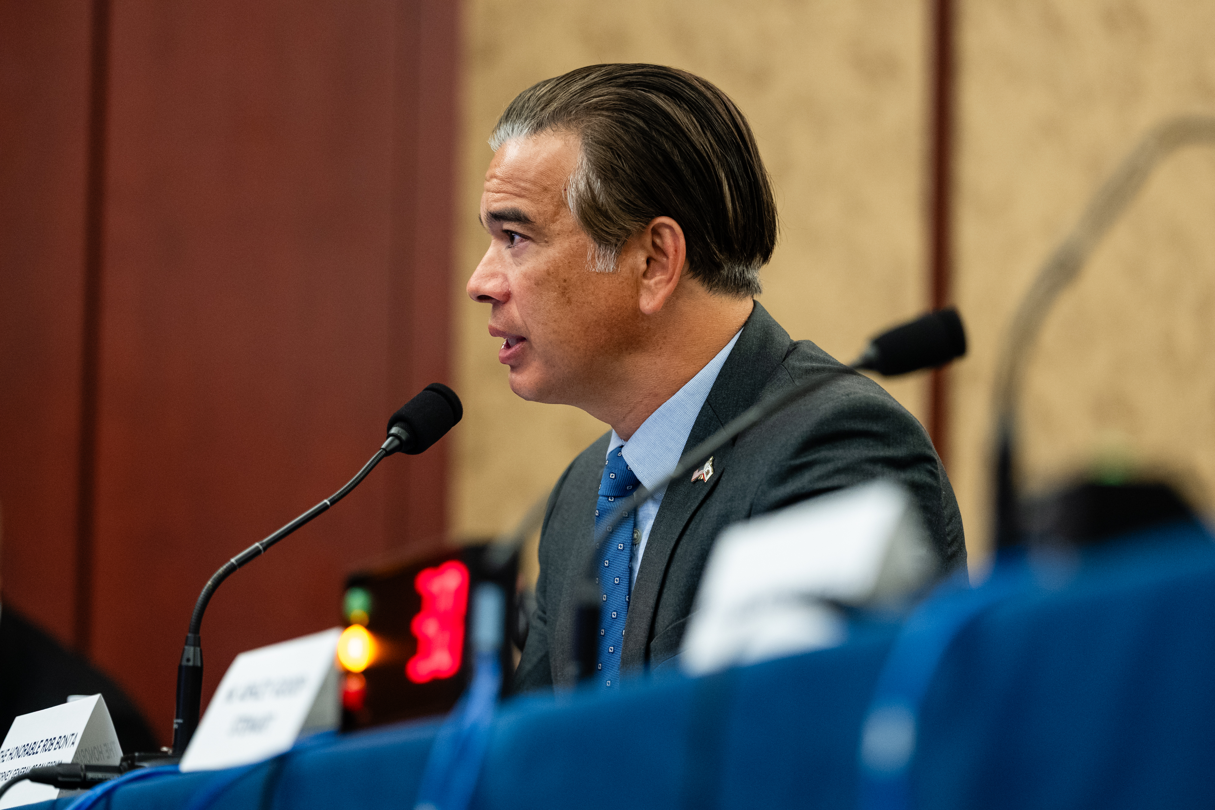 California Attorney General Rob Bonta speaking into a microphone at a congressional hearing table, wearing a gray suit and blue tie.