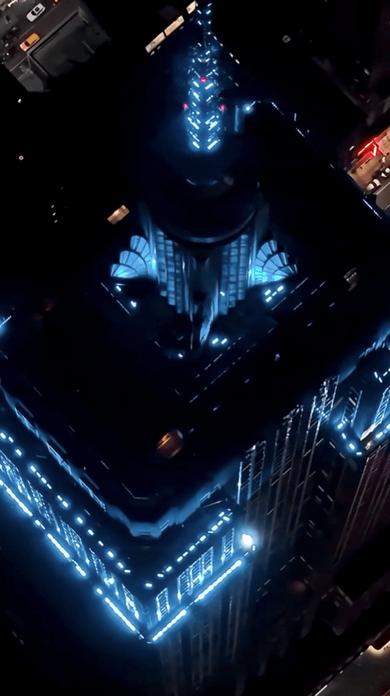 Aerial top-down view of the Empire State Building lit in vivid blue at night, with its Art Deco crown glowing below.
