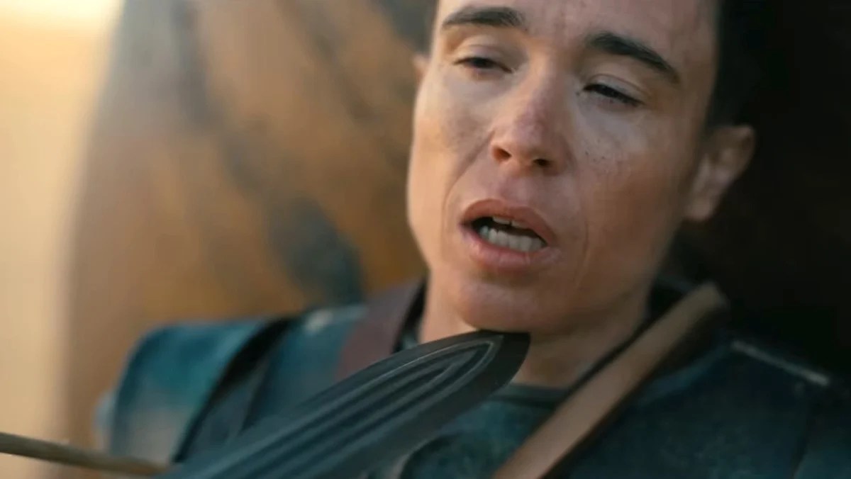 Close-up of a person in dark armor grimacing with eyes half-closed and mouth open.