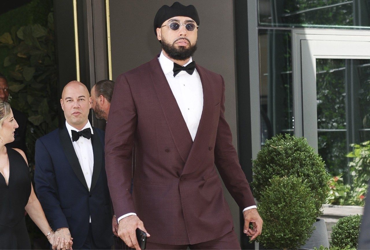 Tall man in a burgundy double-breasted tuxedo with black bow tie, round sunglasses, and black knit cap walking outside in New York City.