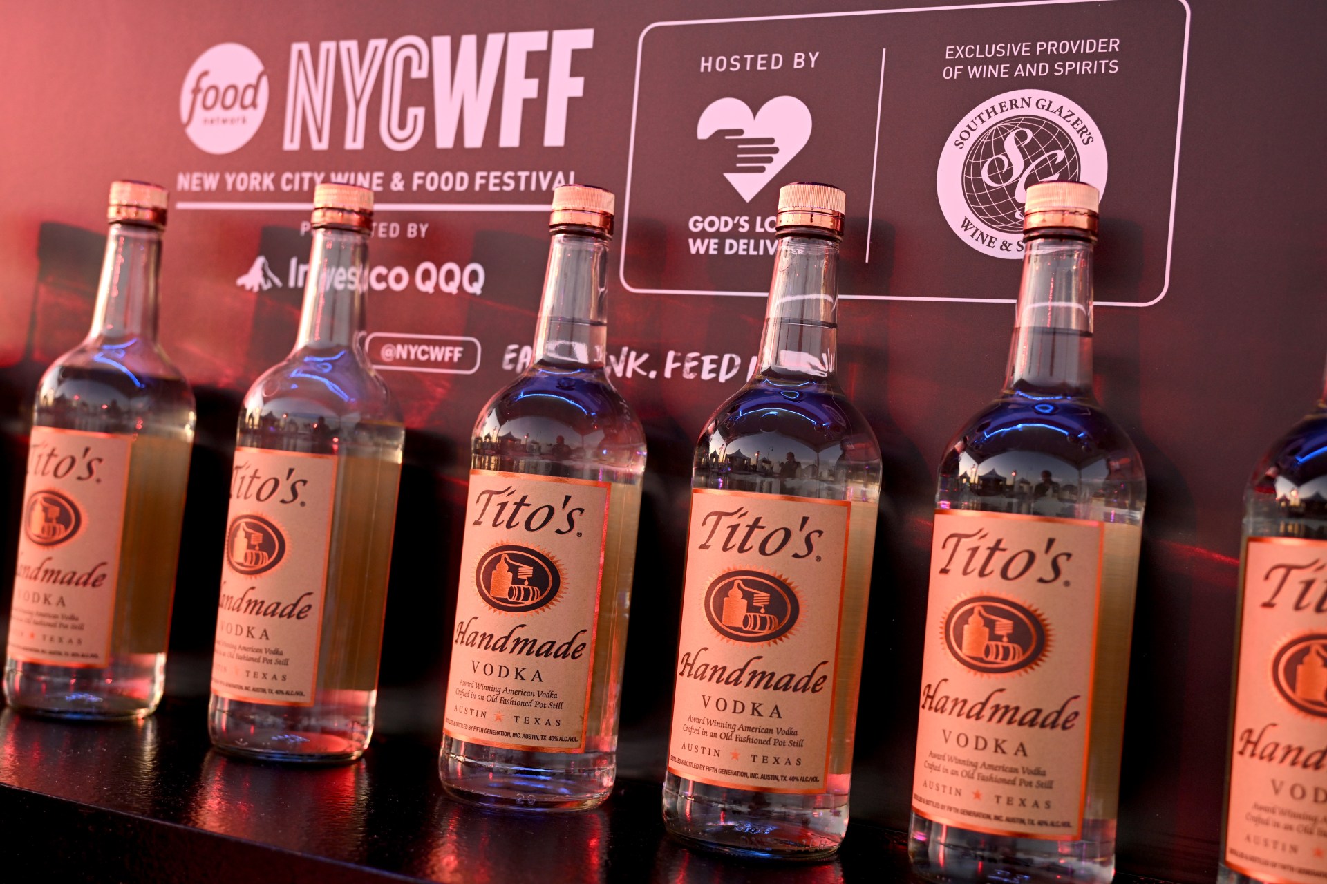 Row of Tito's Handmade Vodka bottles displayed on a shelf in front of an NYCWFF event backdrop.