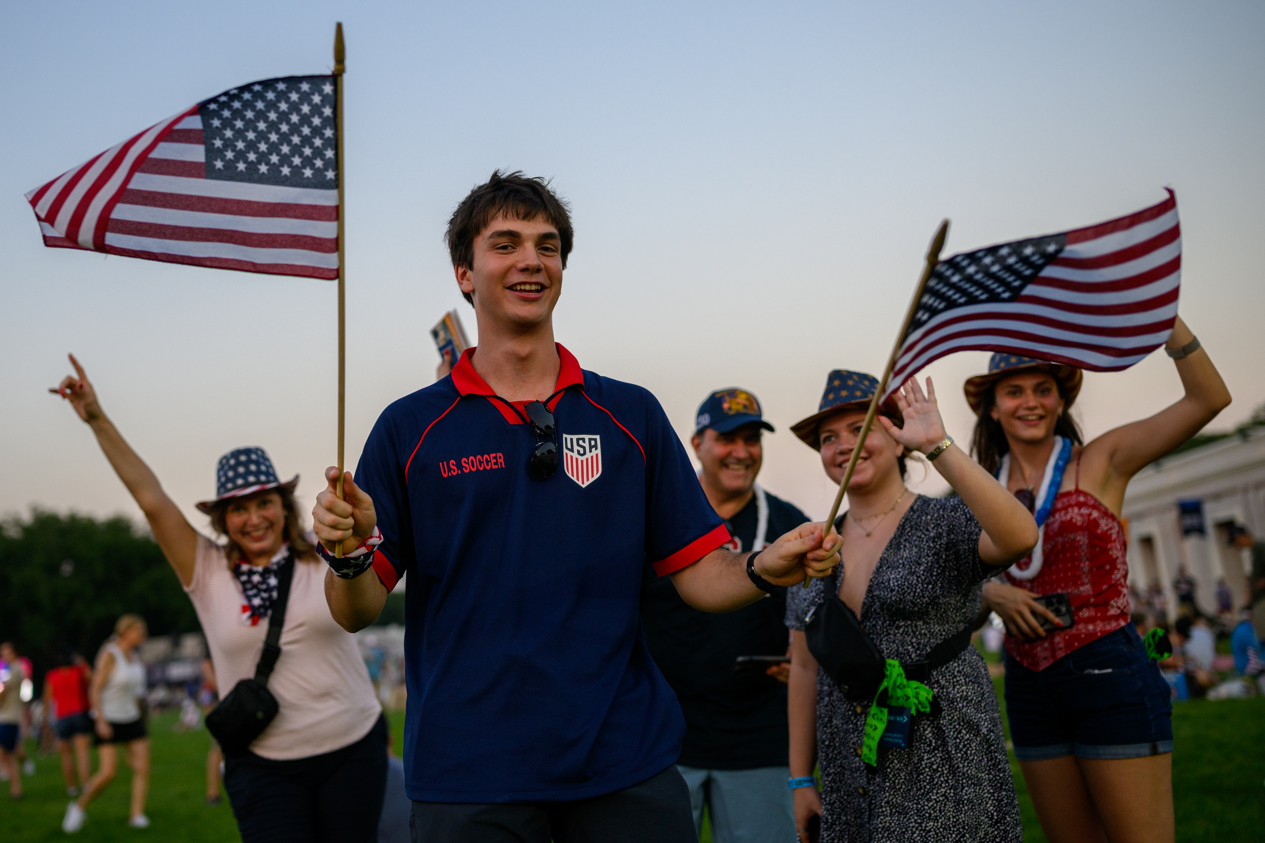 A man waves American flags at the Great American State Fair in Washington, D.C., surrounded by friends posing for photos