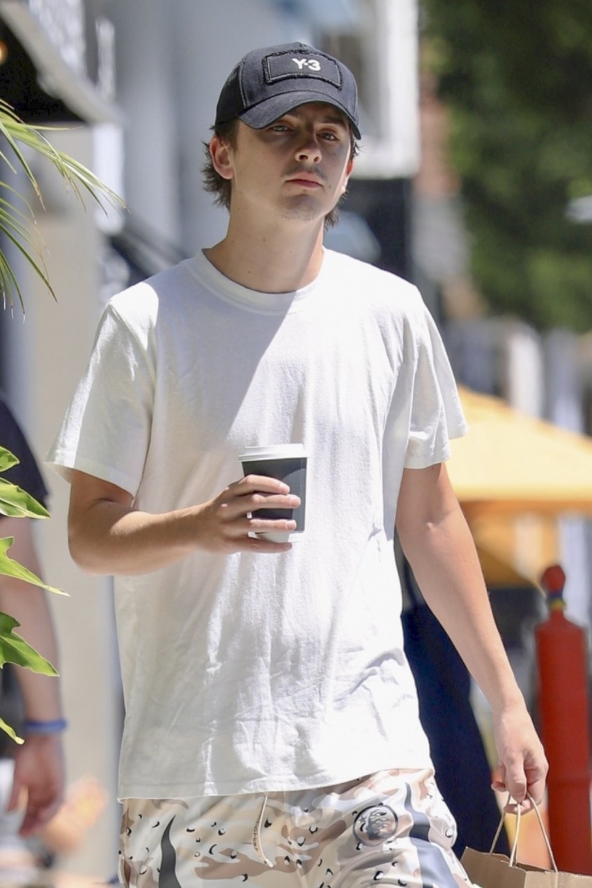 Timothée Chalamet in a white T-shirt, black cap, and white sneakers carrying a coffee and paper bag outside a café in Beverly Hills