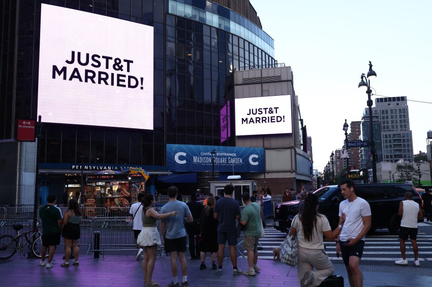 Crowd outside Madison Square Garden watching large screens displaying "JUST&T MARRIED!" celebrating Taylor Swift and Travis Kelce's wedding