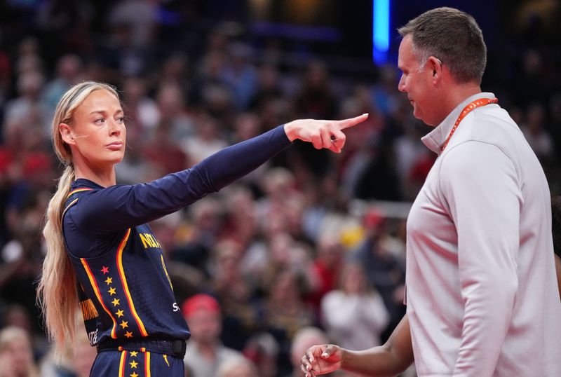 A blonde female basketball player in a navy Indiana Fever uniform points her finger at a man on the sideline in front of a packed arena.