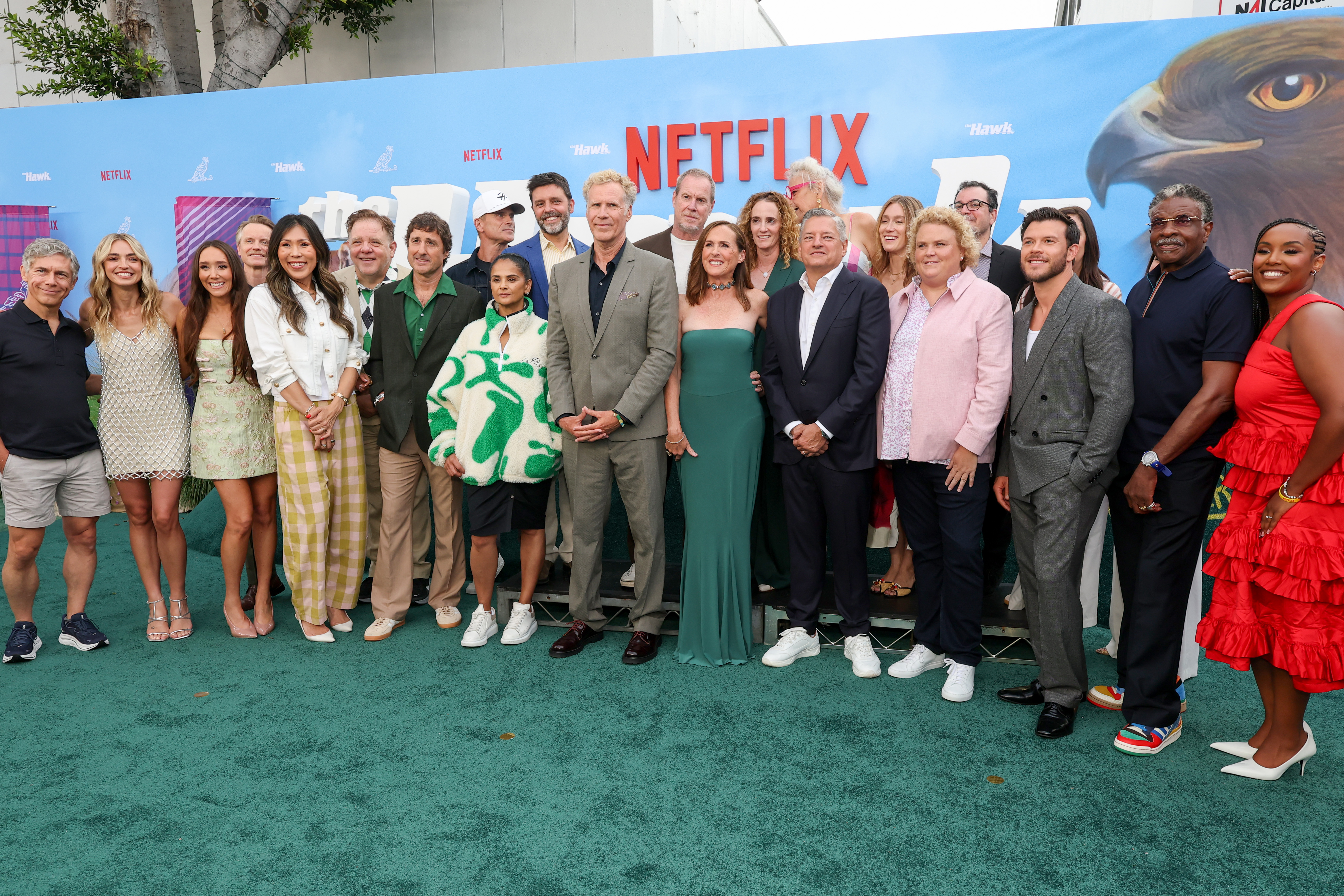 Large group of cast members and Netflix executives posing together on a teal carpet in front of a Netflix 'The Hawk' premiere backdrop in Los Angeles.