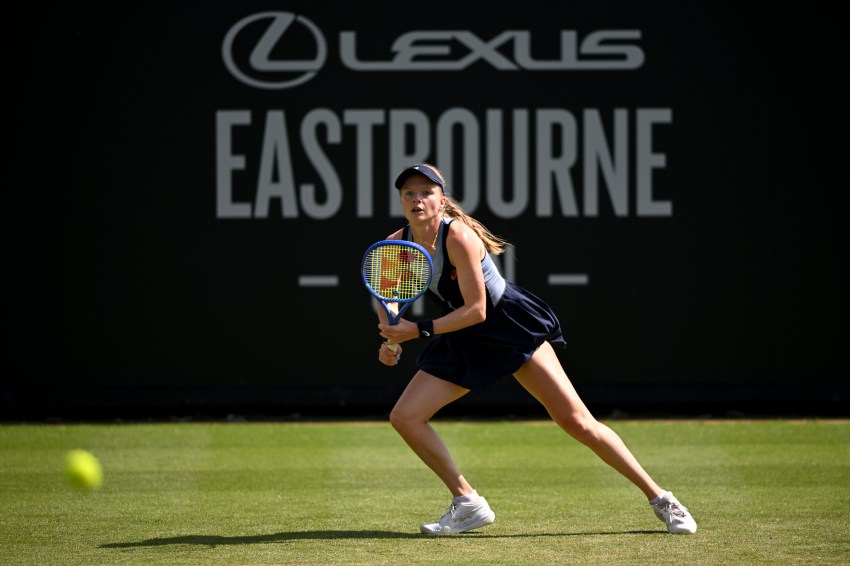 Female tennis player in navy outfit lunging forward on a grass court to return a shot, with a Lexus Eastbourne signboard in the background.