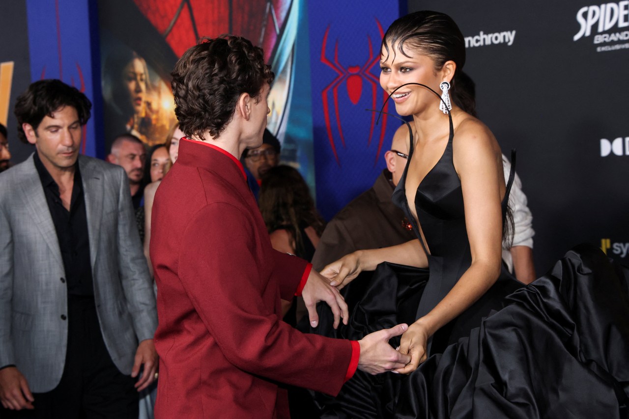Tom Holland in a red suit greets a smiling Zendaya in a black satin gown at the Spider-Man: Brand New Day premiere in Los Angeles.