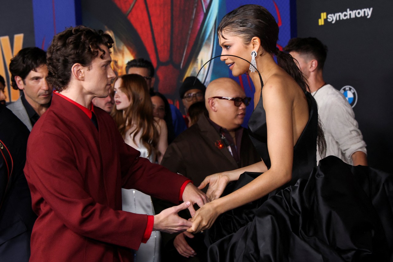 Tom Holland in a red jacket holds hands with Zendaya in a black satin gown at the Spider-Man: Brand New Day premiere in Los Angeles.