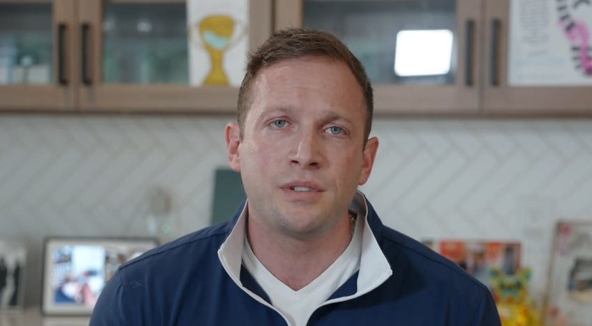 Man in a navy quarter-zip pullover speaking directly to camera in a home kitchen setting