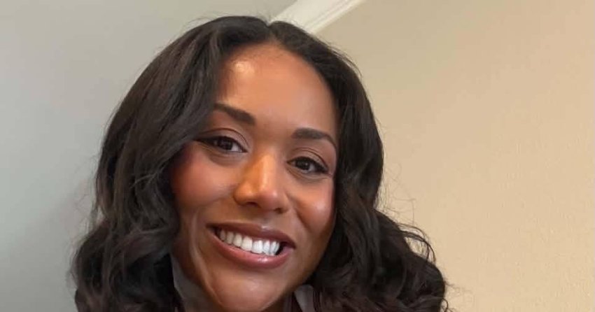 Woman with curly dark hair and a patterned sleeveless top smiling in a selfie indoors.