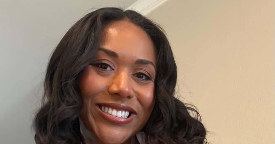 Woman with curly dark hair and a patterned sleeveless top smiling in a selfie indoors.