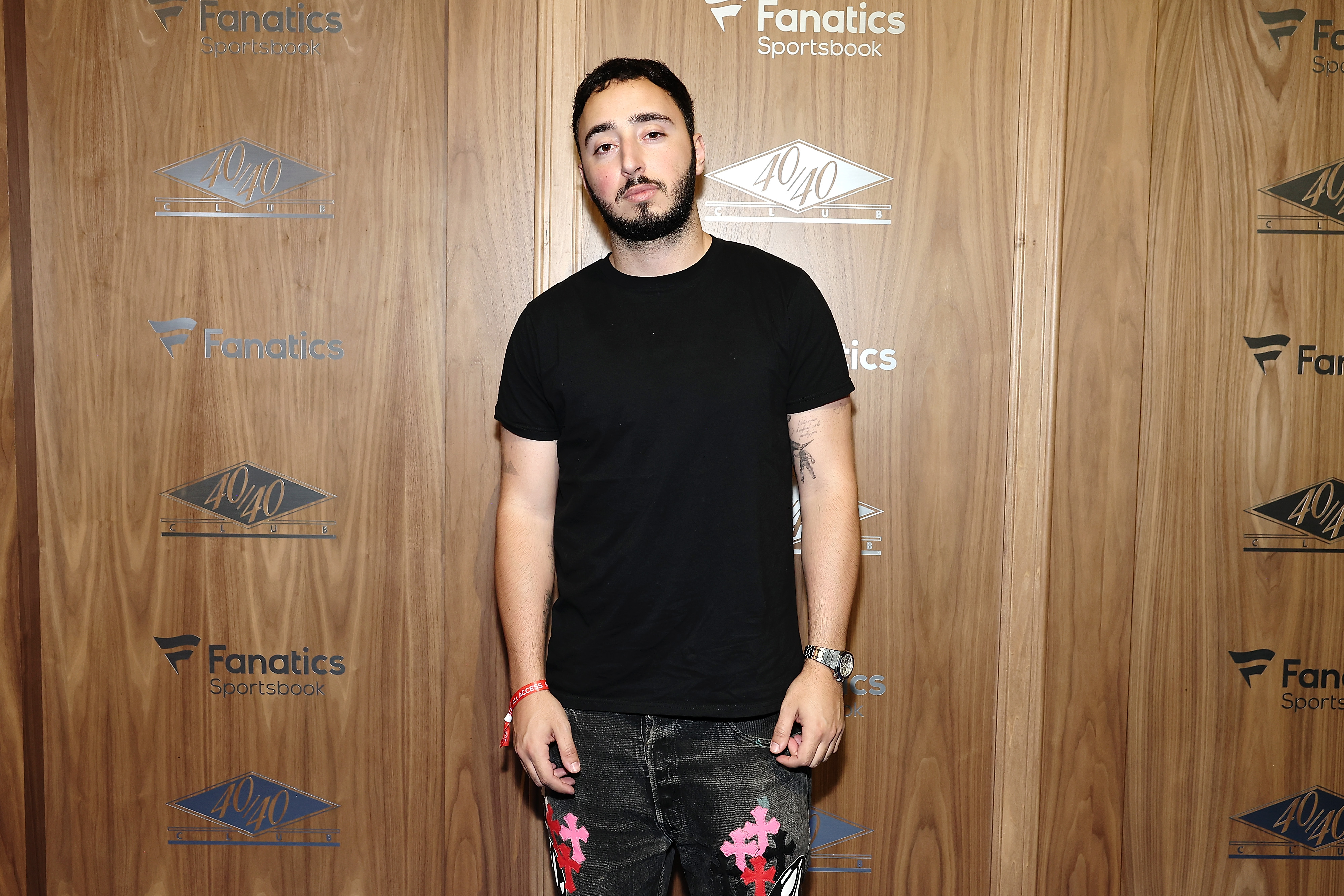 Zack Bia in a black t-shirt and dark jeans standing in front of a Fanatics Sportsbook and 40/40 Club step-and-repeat backdrop.