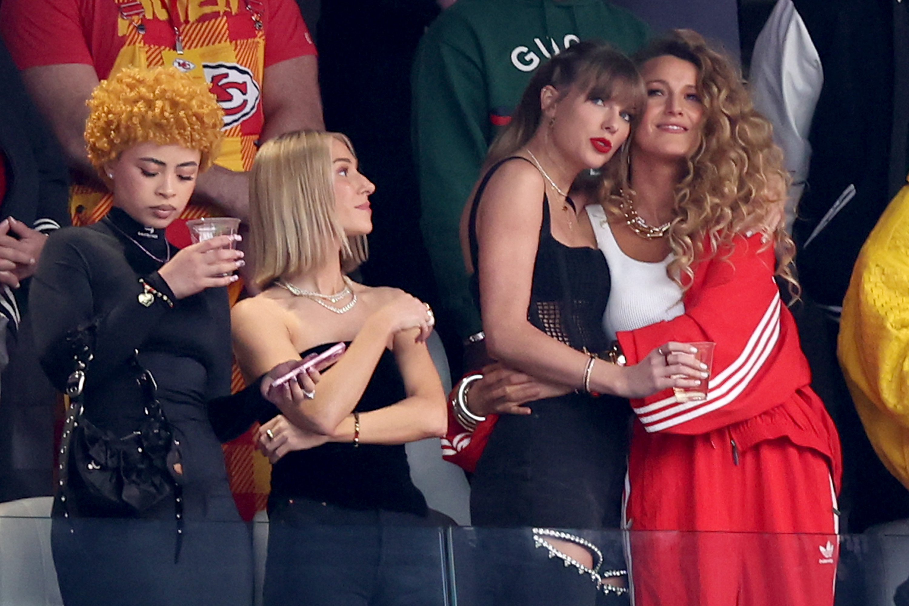 Ice Spice, Taylor Swift, and Blake Lively standing together in stadium seats before Super Bowl LVIII in Las Vegas.