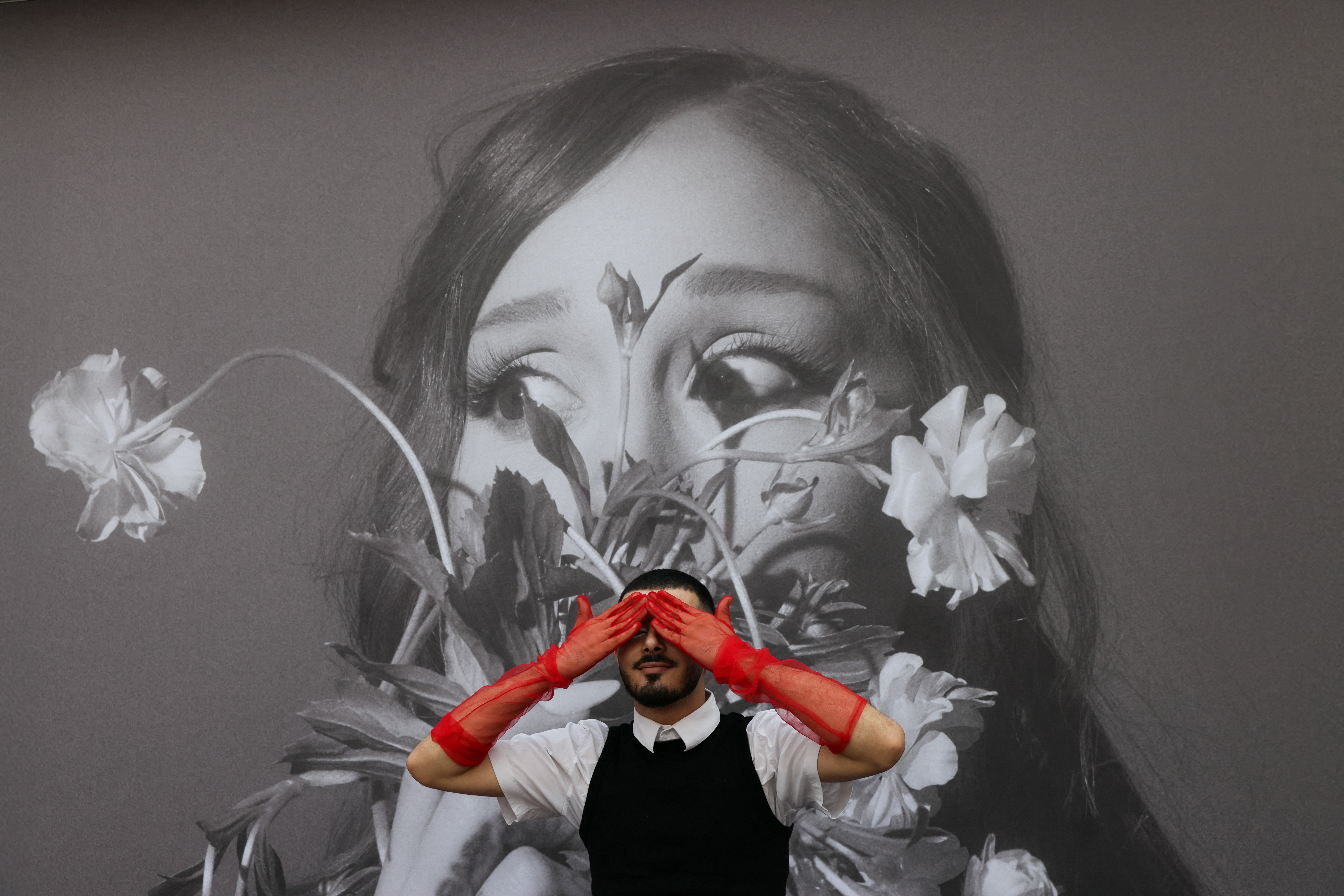 Click to open the image gallery An Ariana Grande fan posing in front of a tour billboard as fans gather outside the venue in London