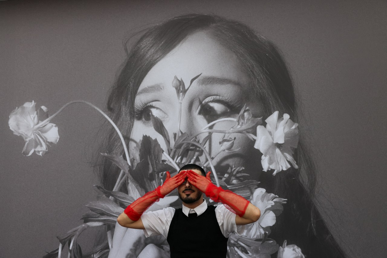 An Ariana Grande fan posing in front of a tour billboard as fans gather outside the venue in London