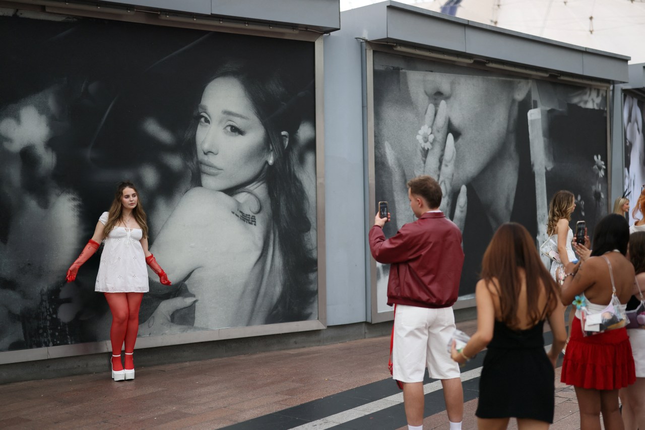 Ariana Grande fans taking pictures in front of an Eternal Sunshine Tour billboard in London