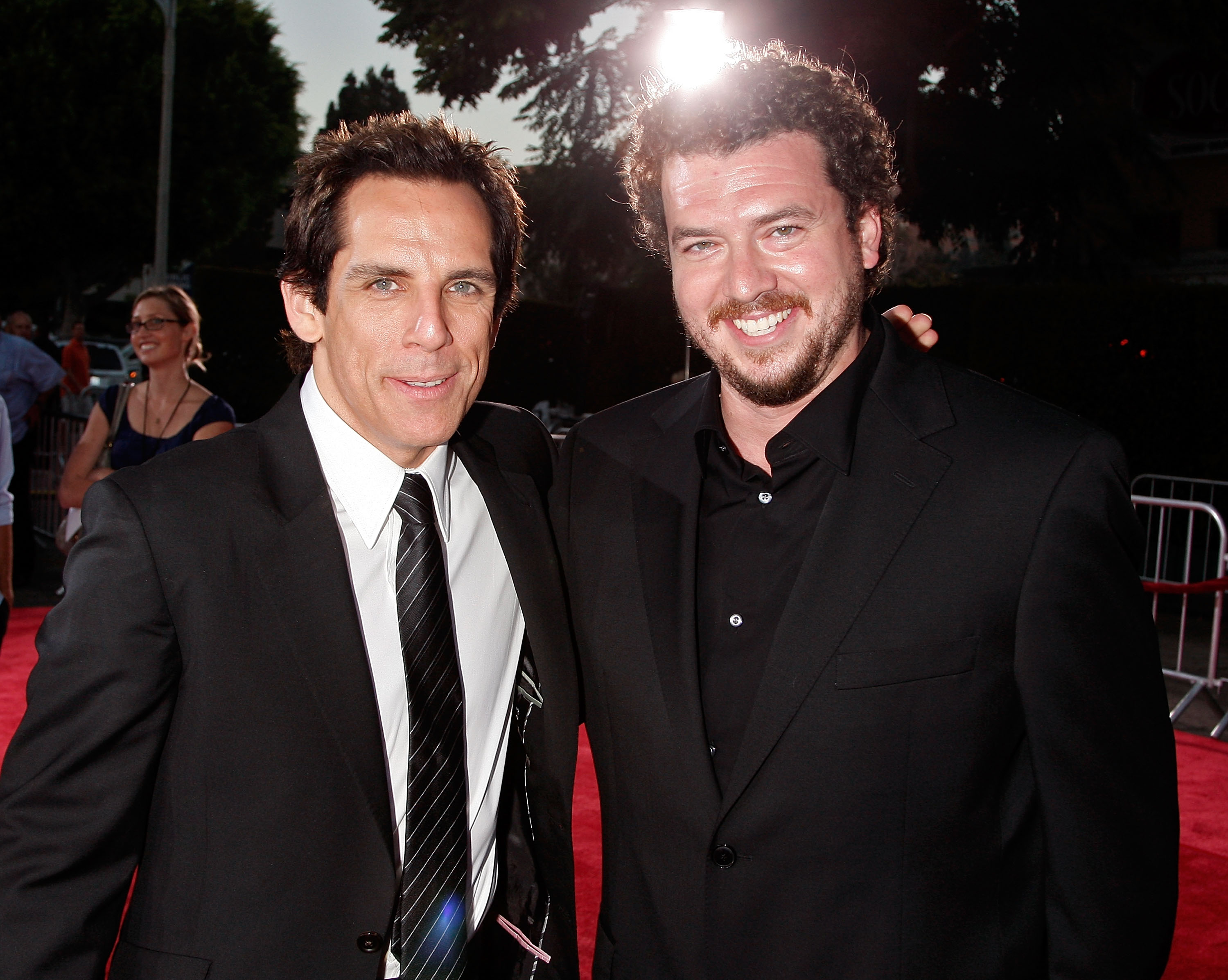 Ben Stiller in a dark suit and tie stands with Danny McBride in an all-black outfit on a red carpet at the Tropic Thunder premiere.