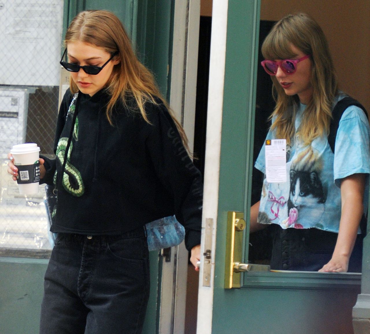 Two young women leaving a building — one in a black snake-print hoodie holding a coffee cup, the other in a blue cat-print T-shirt wearing pink sunglasses.