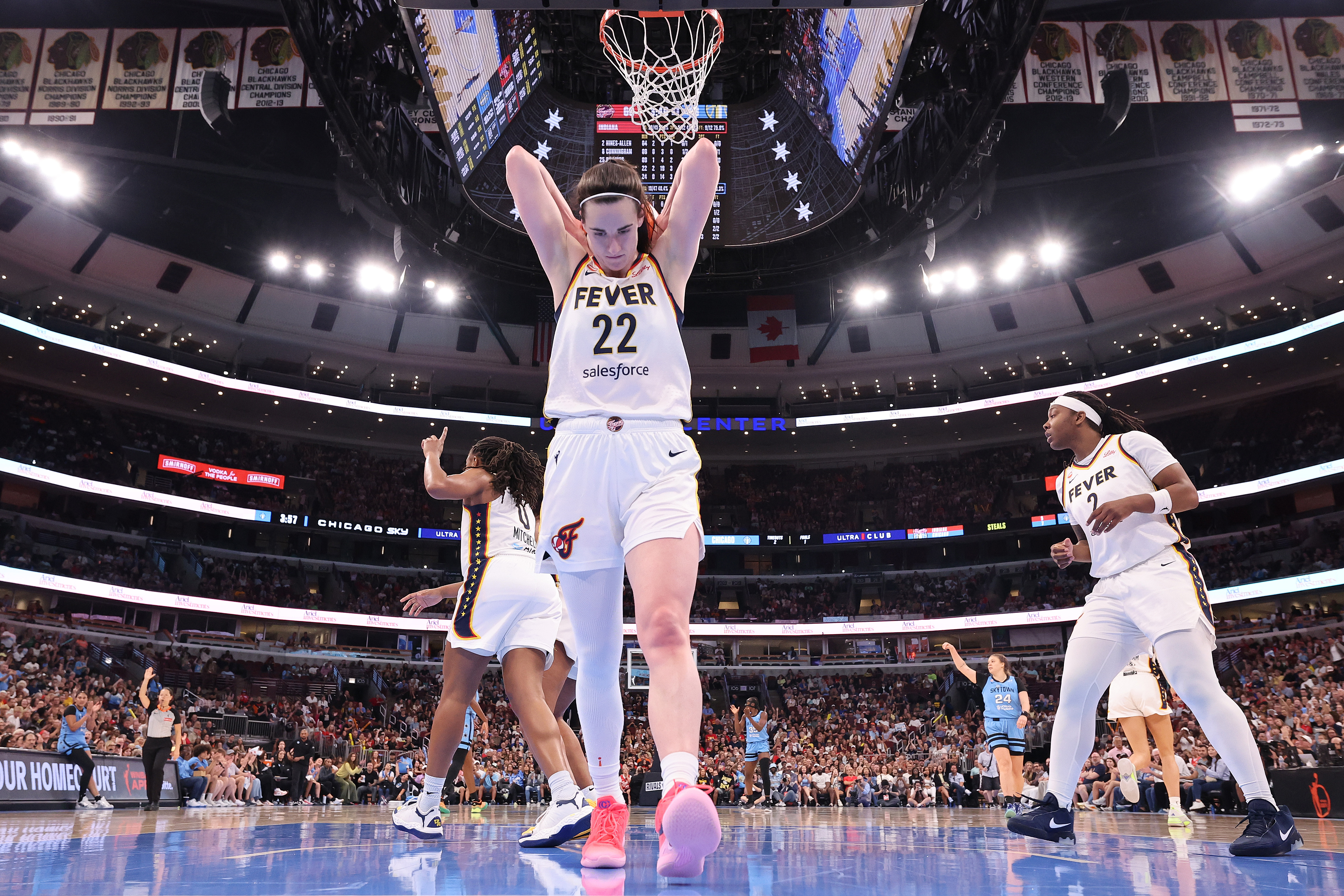 Caitlin Clark, wearing Indiana Fever jersey number 22, hangs from the basketball rim at United Center in Chicago during a game against the Chicago Sky.