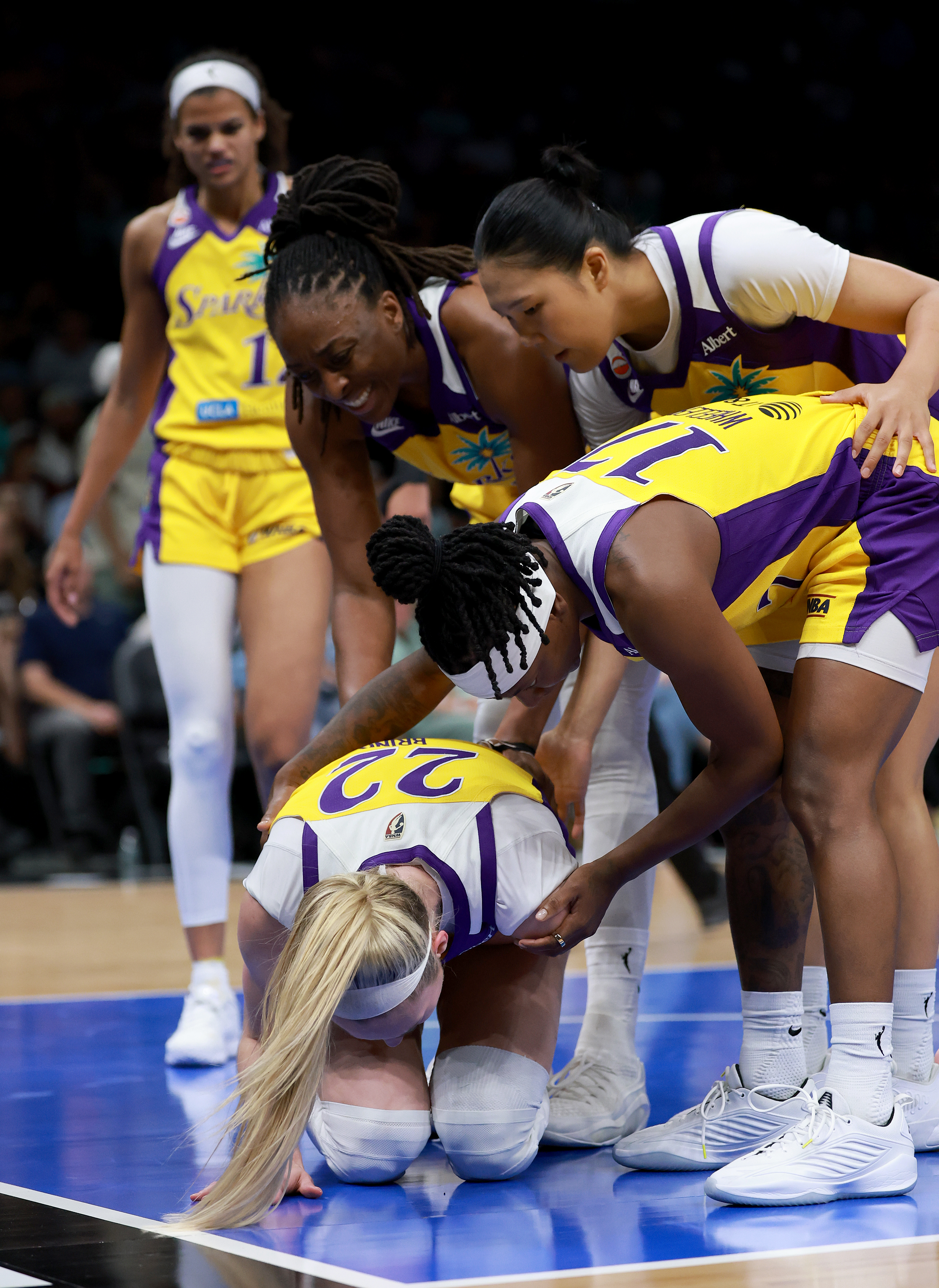 Cameron Brink #22 is on her knees on the court while three LA Sparks teammates crouch around her to help during a WNBA game.