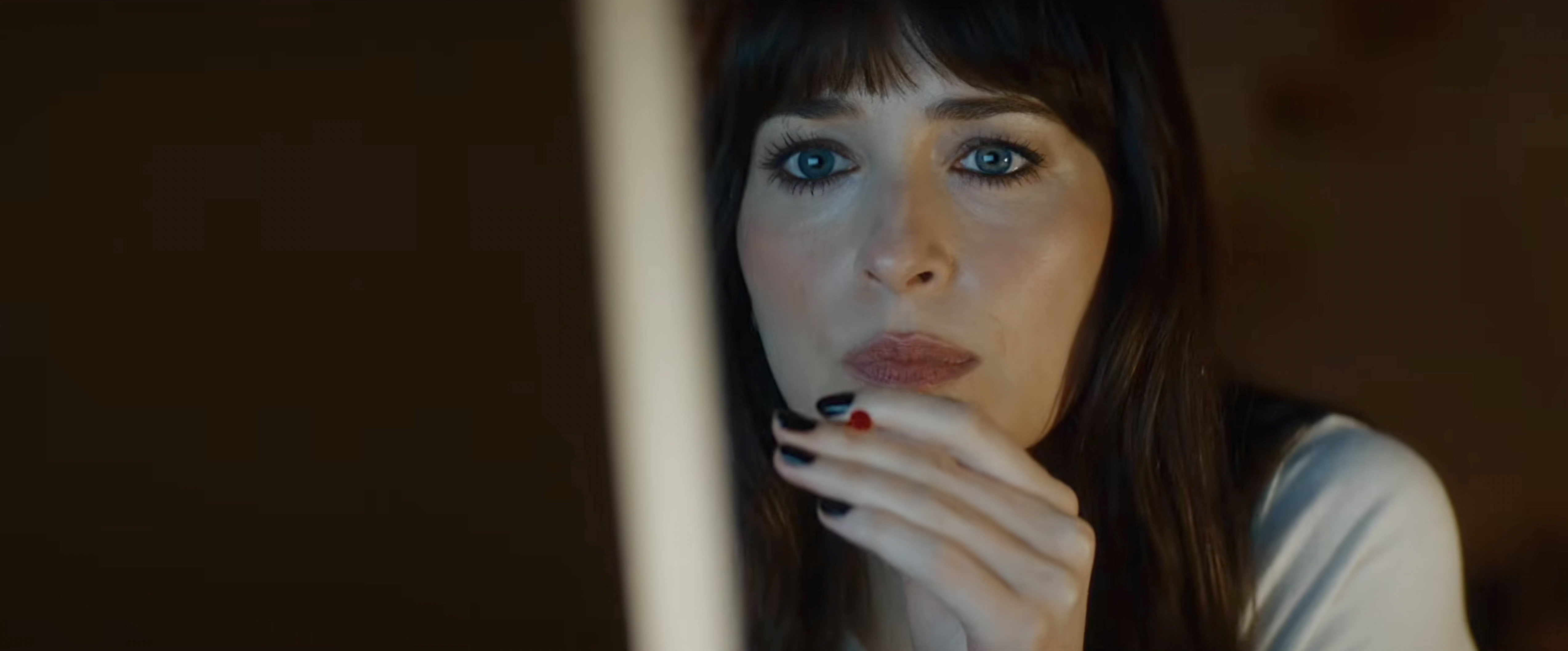 Close-up of a dark-haired blue-eyed woman resting her chin on her hand, looking pensive, with black and red nail polish.