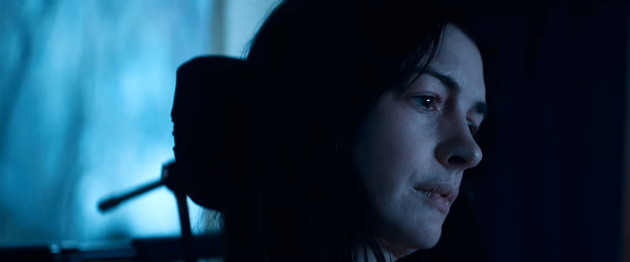 Close-up profile of a dark-haired woman illuminated by dim blue light, gazing off to the side with a pensive expression.