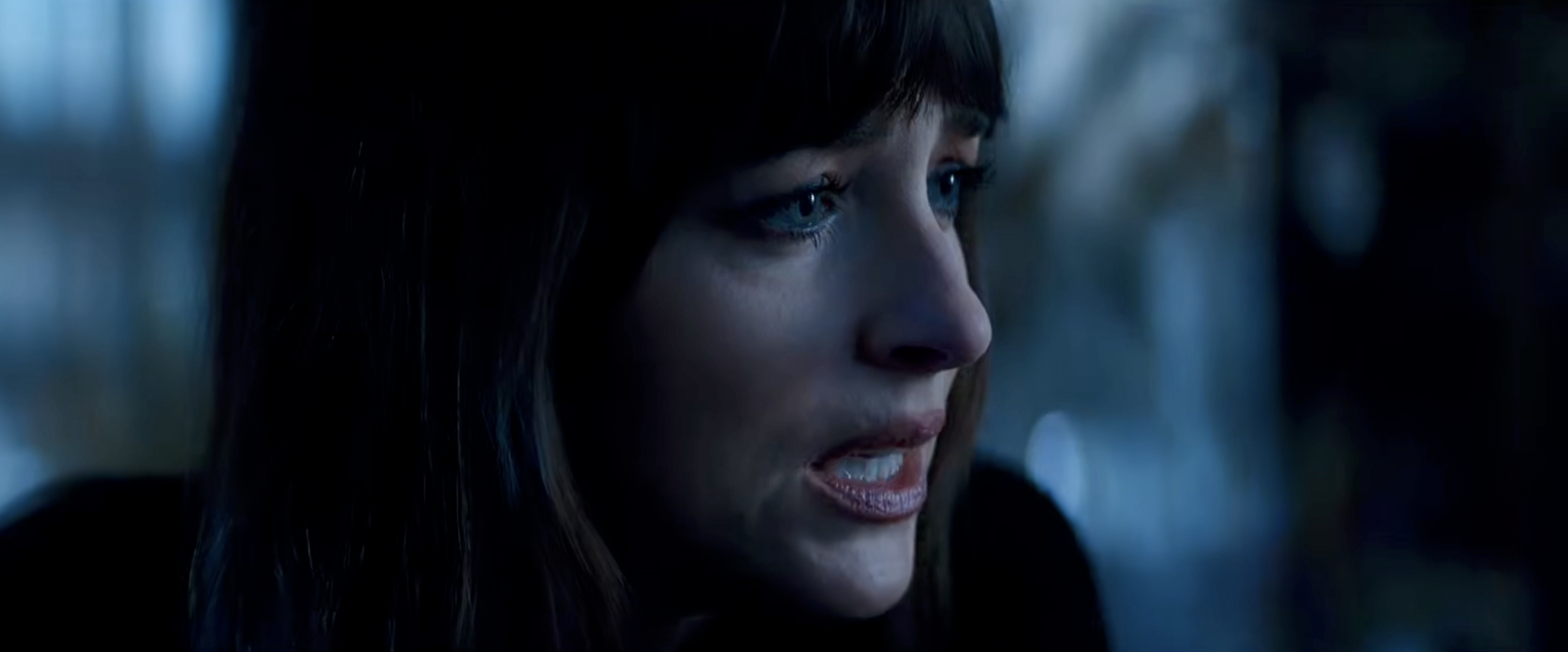 Close-up of a dark-haired woman with bangs looking off to the side in dim blue lighting.