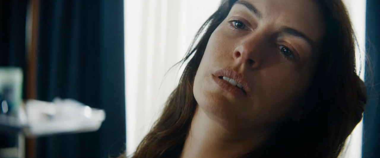Close-up of a young woman with long dark hair looking upward with a pensive expression, soft light behind her.