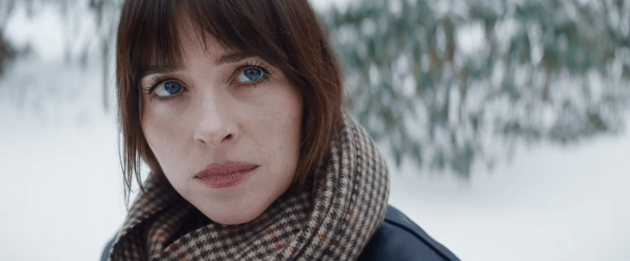 Close-up of a dark-haired woman with blue eyes wearing a plaid scarf outdoors in a snowy setting.