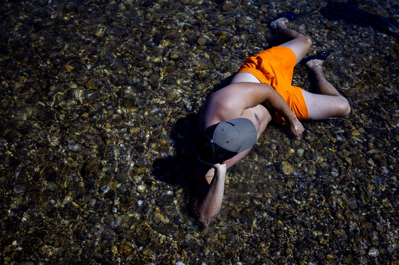 A man lying on the shallow, exposed bed of the Danube River near Hainburg an der Donau, Austria, during a heatwave