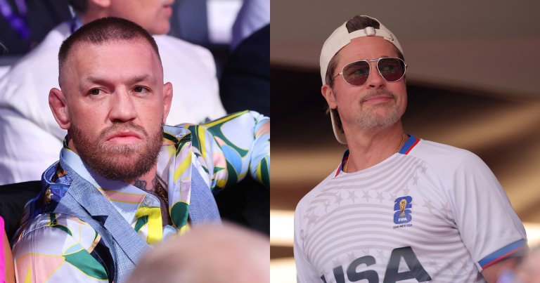 Conor McGregor seated ringside at Wembley Stadium, wearing a colorful patterned shirt over a blue jacket, with a serious expression.