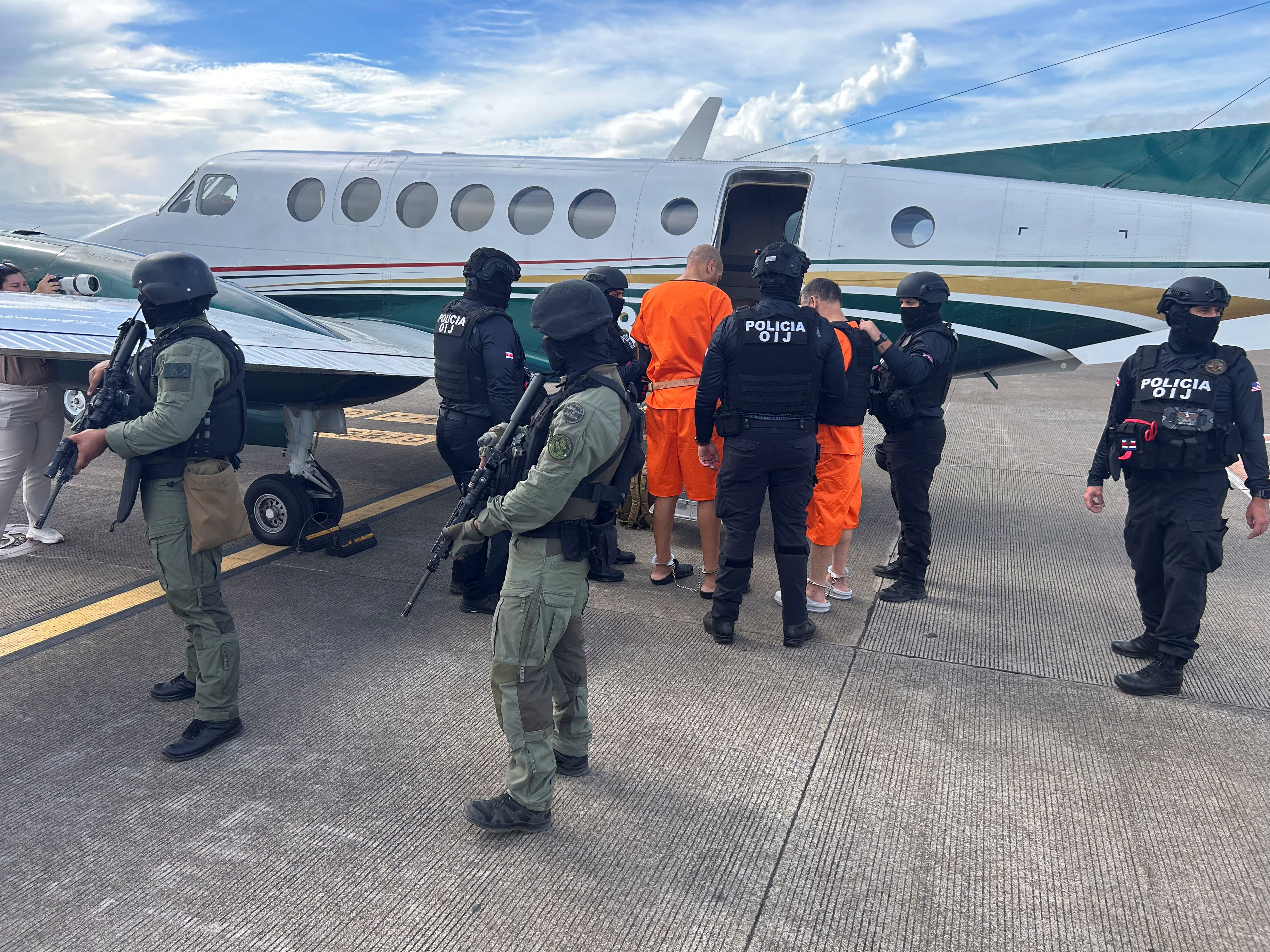 Costa Rican security forces escorting two handcuffed men through an airport before extradition to the United States